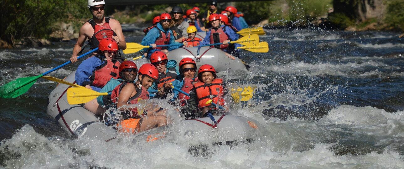 Group of people whitewater rafting with paddle splashes on a river, wearing safety gear.